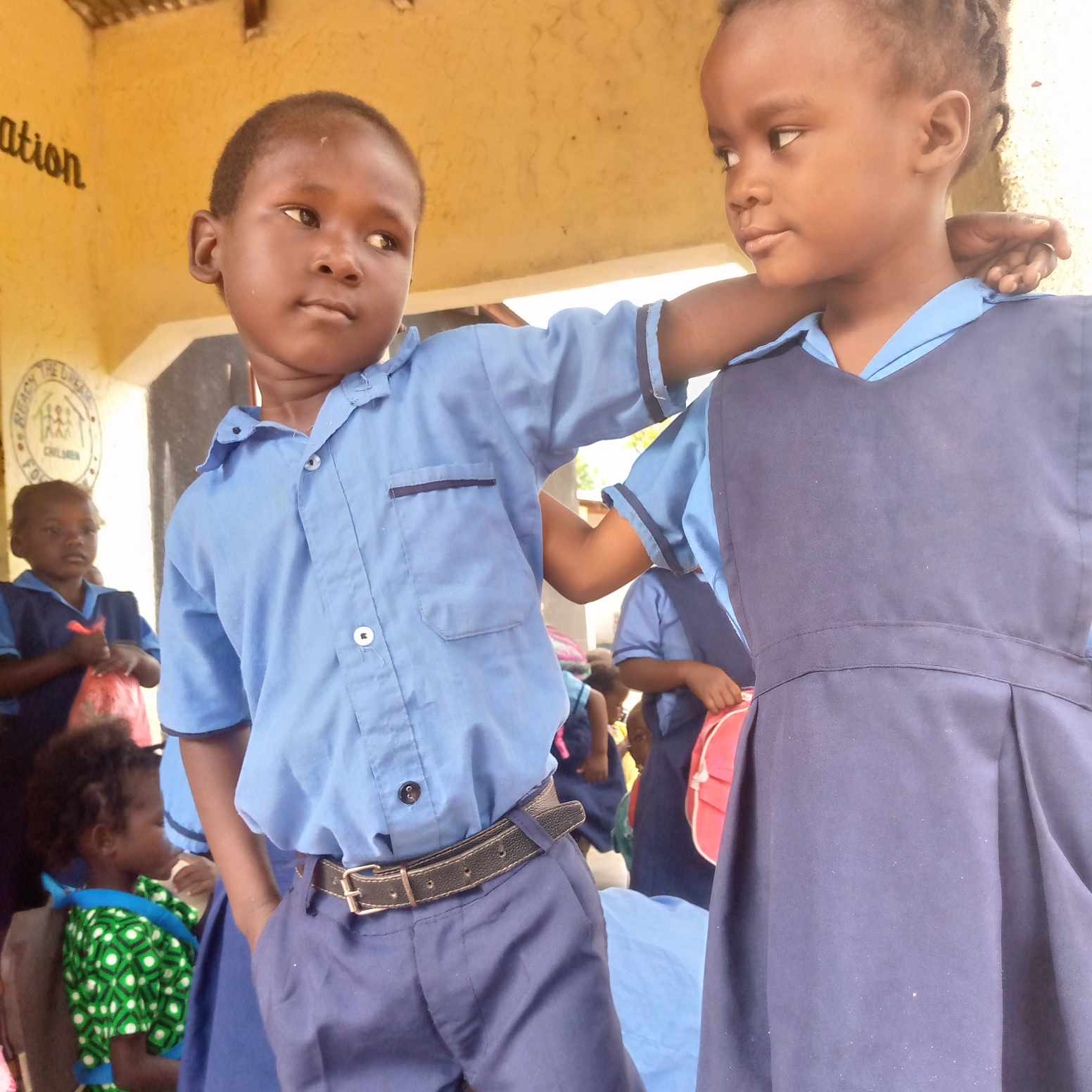 Two young Malawian students in blue uniforms, a boy with his arm around a girl's shoulder.